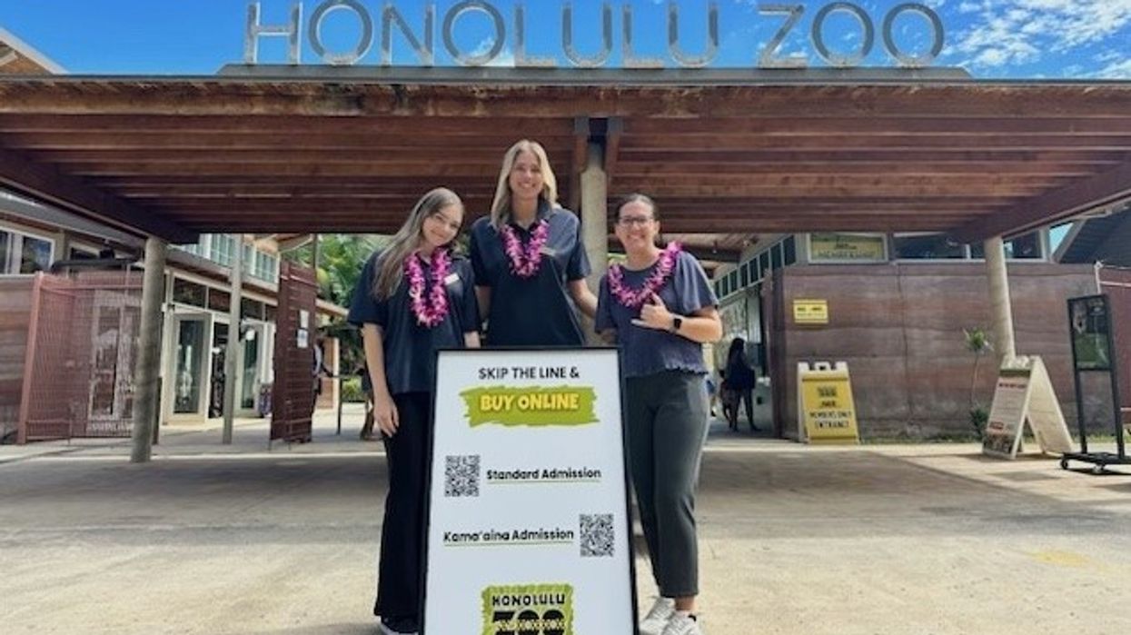 Three people in leis smiling at Honolulu Zoo entrance beside a sign about buying tickets online.