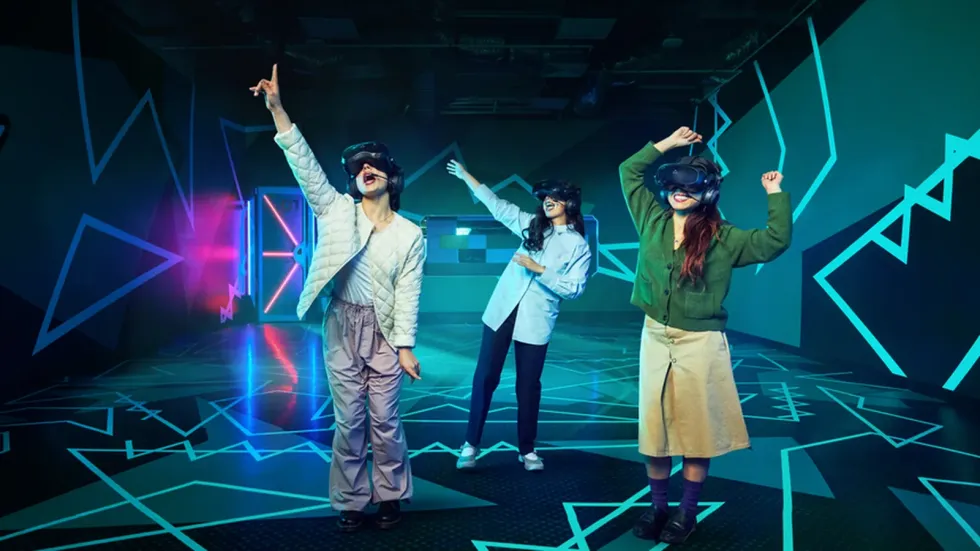 Three people in VR headsets interact energetically in a neon-lit virtual reality room.
