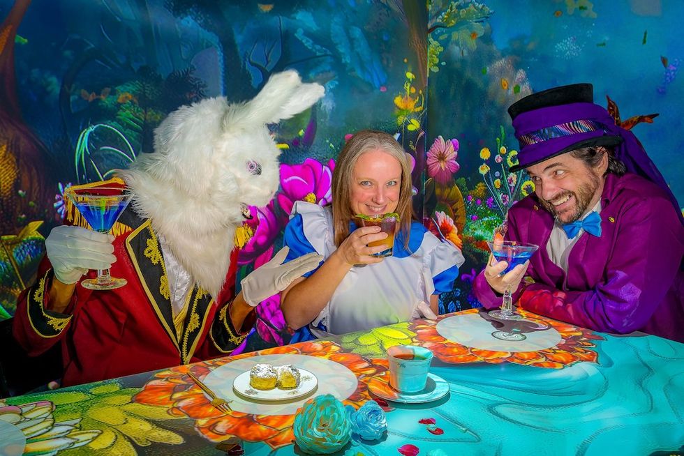 Three people in whimsical costumes at a colorful, fantasy-themed tea party.