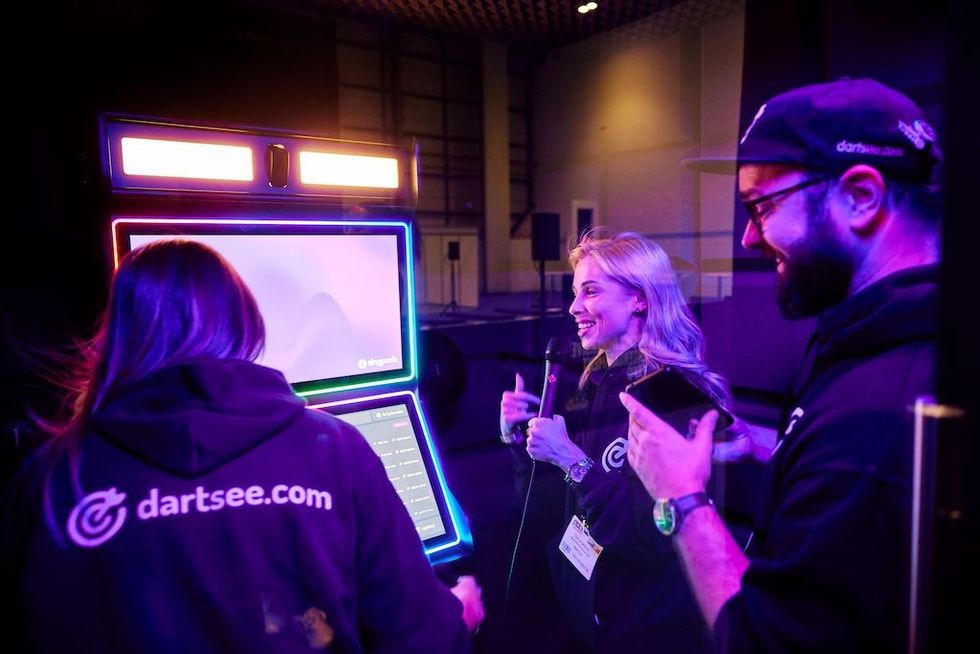 Three people interacting with a neon-lit digital kiosk indoors.