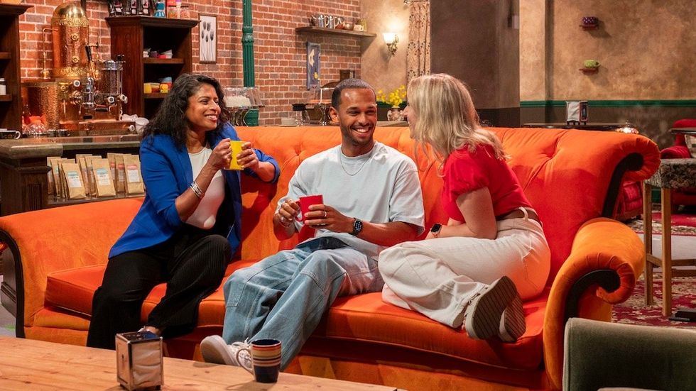 Three people laughing and chatting on the famous Friends orange sofa in replica of Central Perk cafe from the TV show