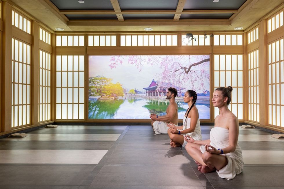 Three people meditating in a serene, Japanese-style room with a nature mural at Suntago Water World.