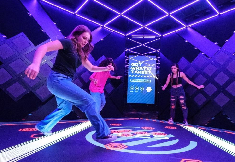 Three people play an interactive floor game under purple lights.
