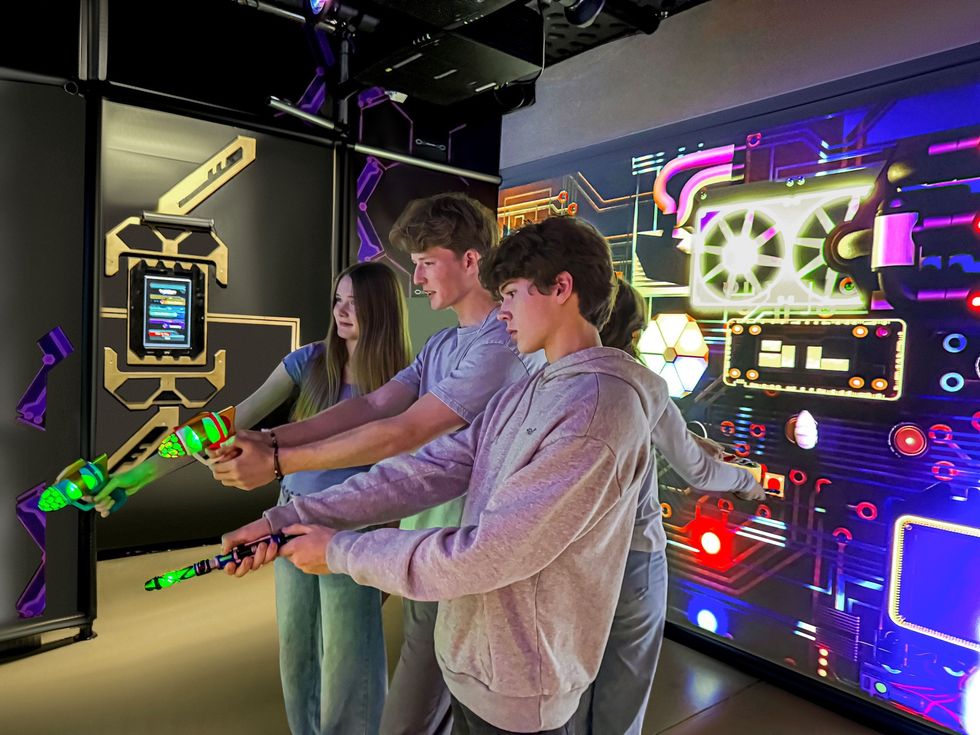 Three people playing an interactive laser game in a neon-lit arcade room.