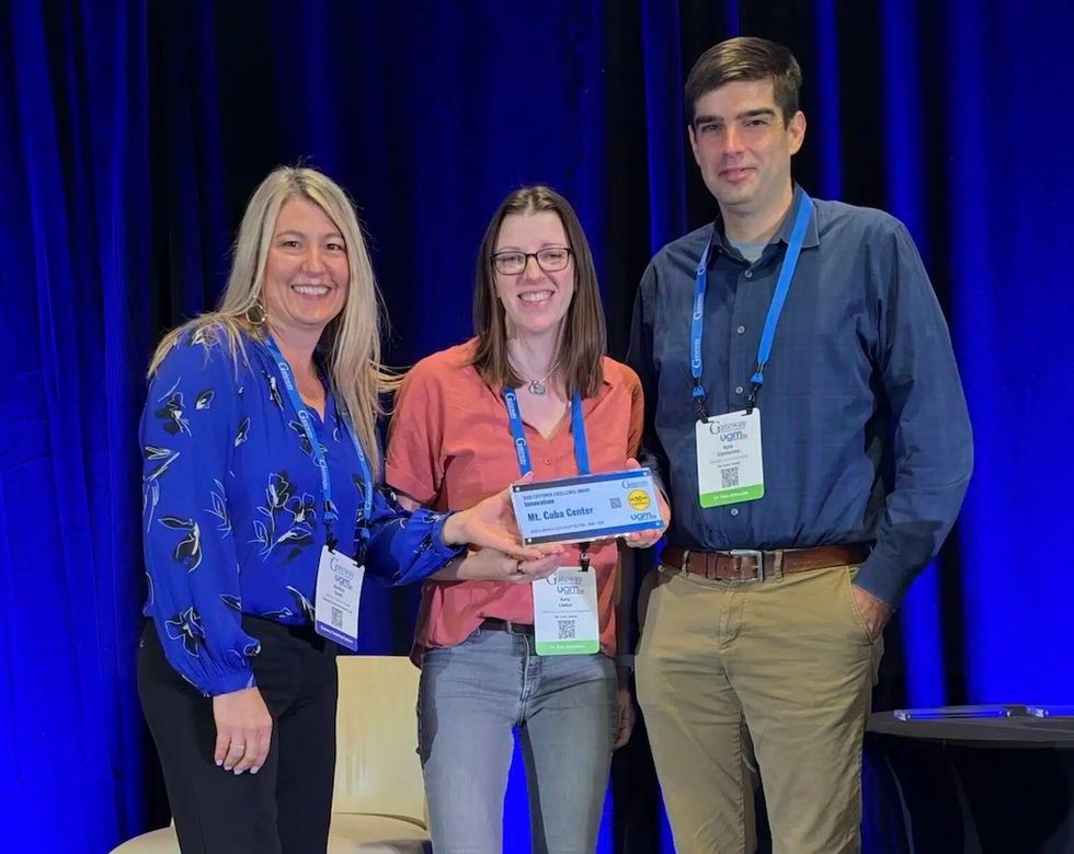 Three people pose with a blue award in front of a dark blue backdrop at Gateway Ticketing's North America UGM Customer Excellence Awards 2026