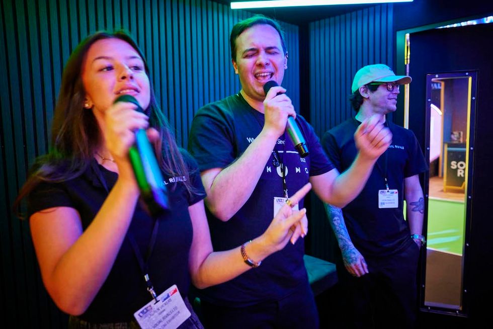 Three people singing karaoke enthusiastically in a neon-lit room.