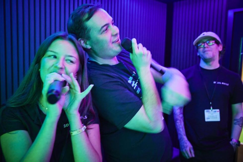 Three people singing with microphones under colorful lights at a karaoke event.