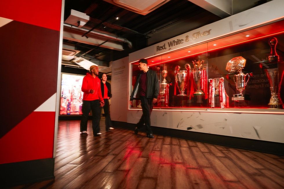 Three people viewing a trophy display titled "Red, White & Silver" in a museum gallery.