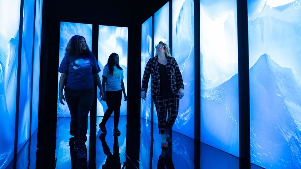 Three people walk through a hallway with glowing blue screens on both sides in Titanic: An Immersive Voyage.
