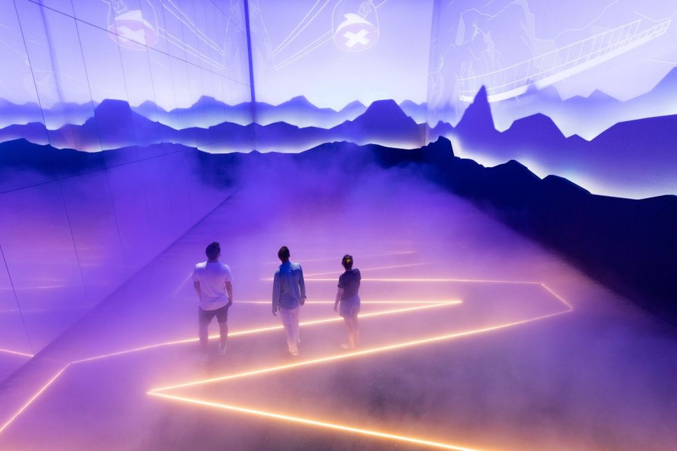 Three people walk through a purple-lit foggy room with digital mountain graphics.