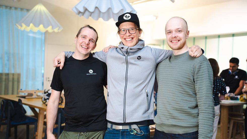 Three smiling men, Leo Holsti, Dr. Raine Kajastila, and Joni V\u00e4h\u00e4m\u00e4ki, standing together in a brightly lit room.