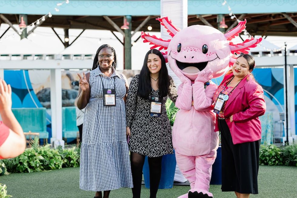 Three women and an axolotl mascot pose happily outdoors.