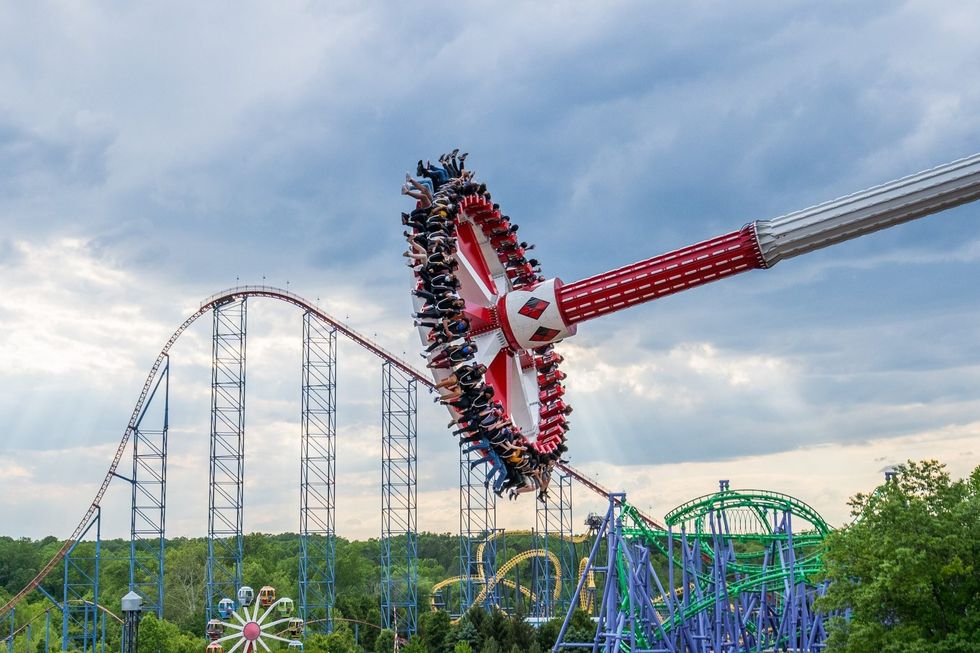 Thrill ride swings near roller coaster under cloudy sky at an amusement park.