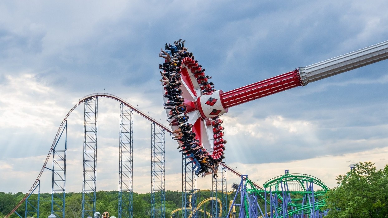 Thrill ride swings passengers against a dramatic sky, with roller coasters in the background.
