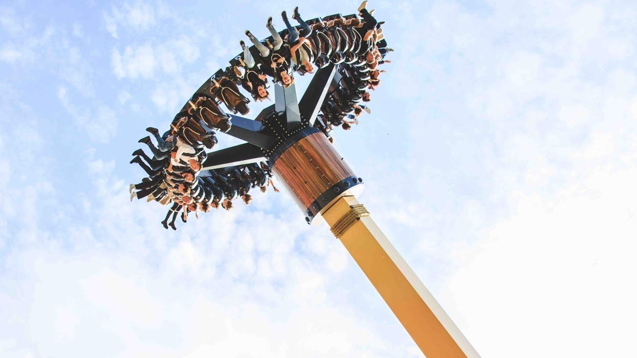 Thrill ride with passengers suspended high against a clear blue sky.