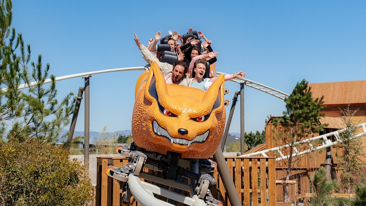 Thrilled riders on an orange-themed roller coaster under a clear blue sky.