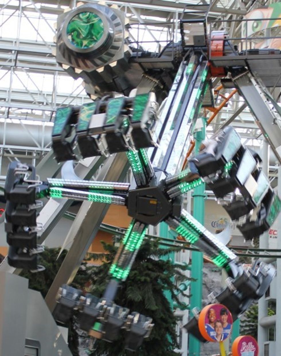 Thrilling indoor amusement ride with rotating, illuminated green arms.