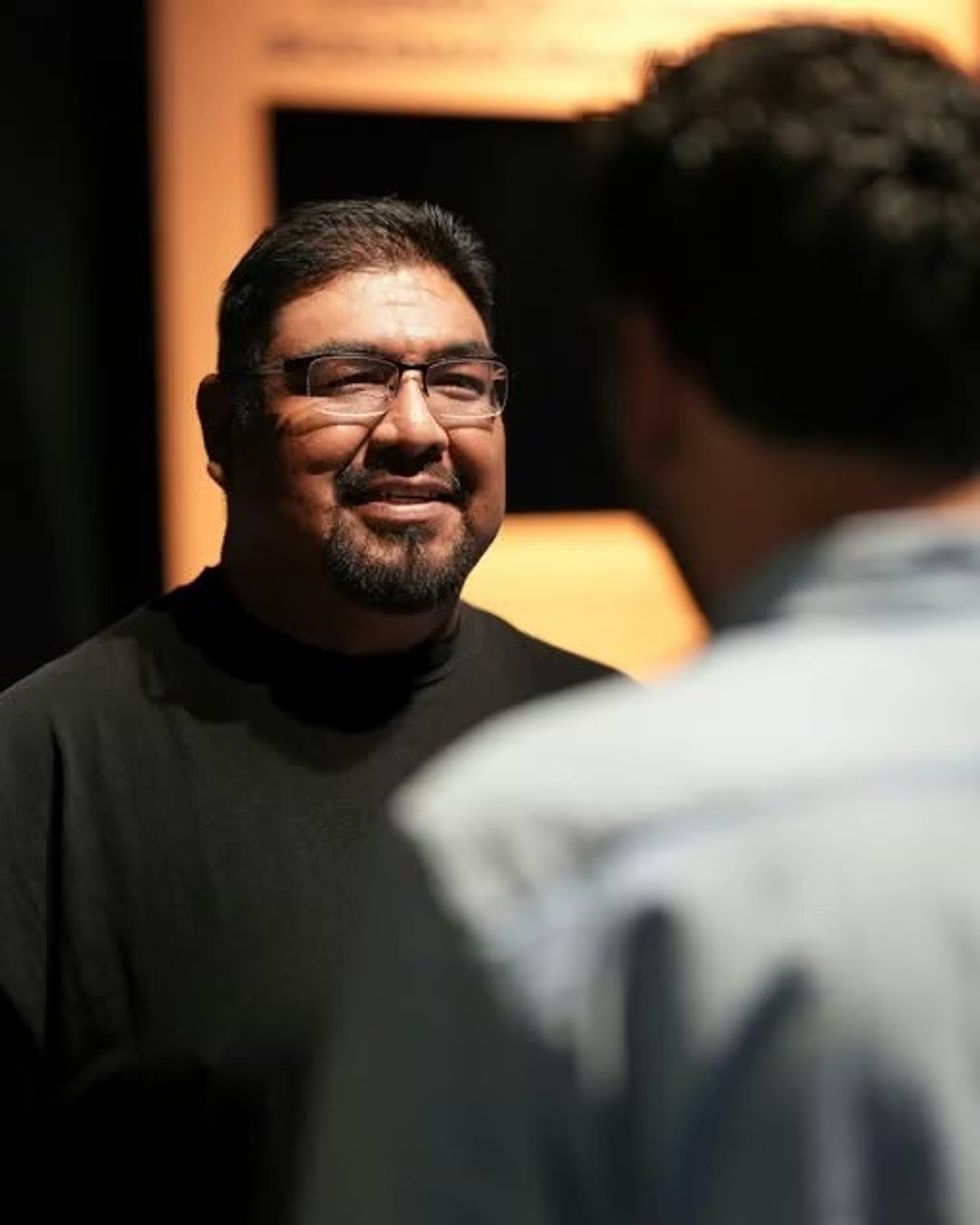 THRIVE \u2014 The First People: Yesterday, Today, and Forever. A man in glasses and a black shirt smiles, engaging in conversation with another person.