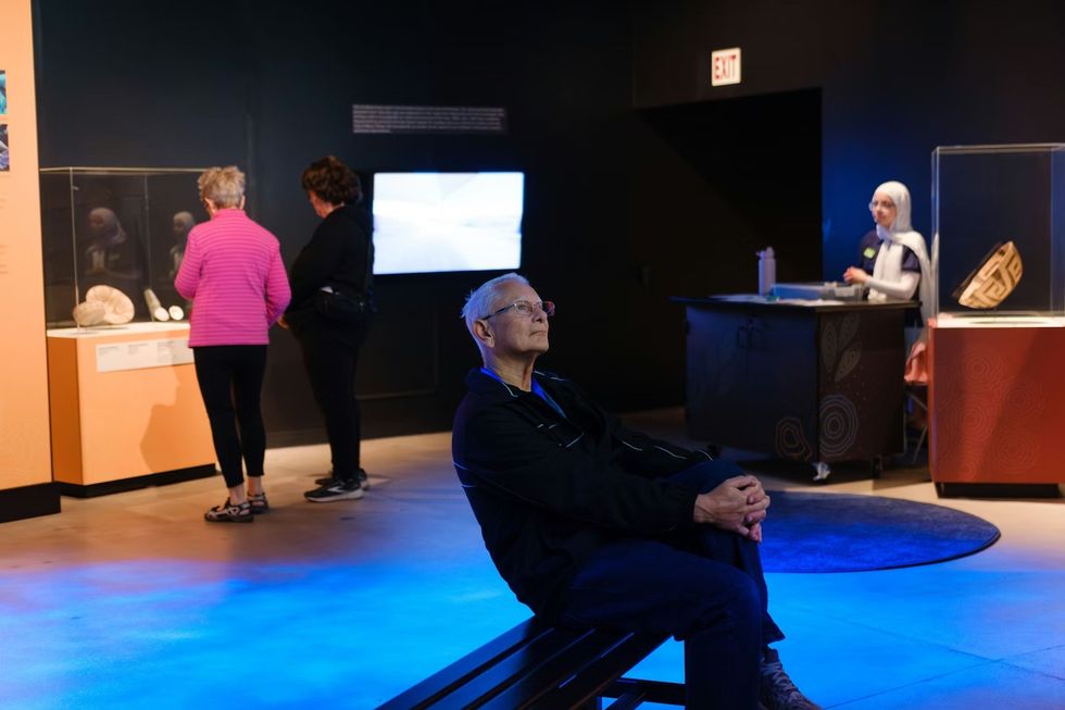 THRIVE \u2014 The First People: Yesterday, Today, and Forever. People exploring a dimly lit museum exhibit with various artifacts displayed.