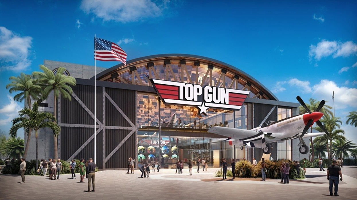Top Gun-themed hangar with a vintage plane and an American flag, surrounded by people.