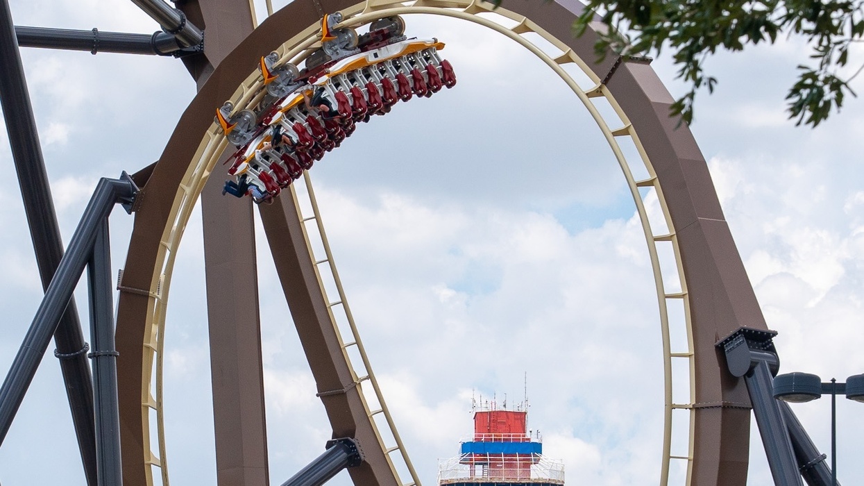 Tormenta Rampaging Run roller coaster loop with riders upside down against a cloudy sky.