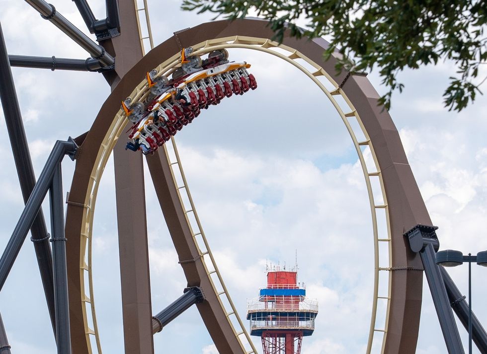 Tormenta Rampaging Run roller coaster loop with riders upside down against a cloudy sky.