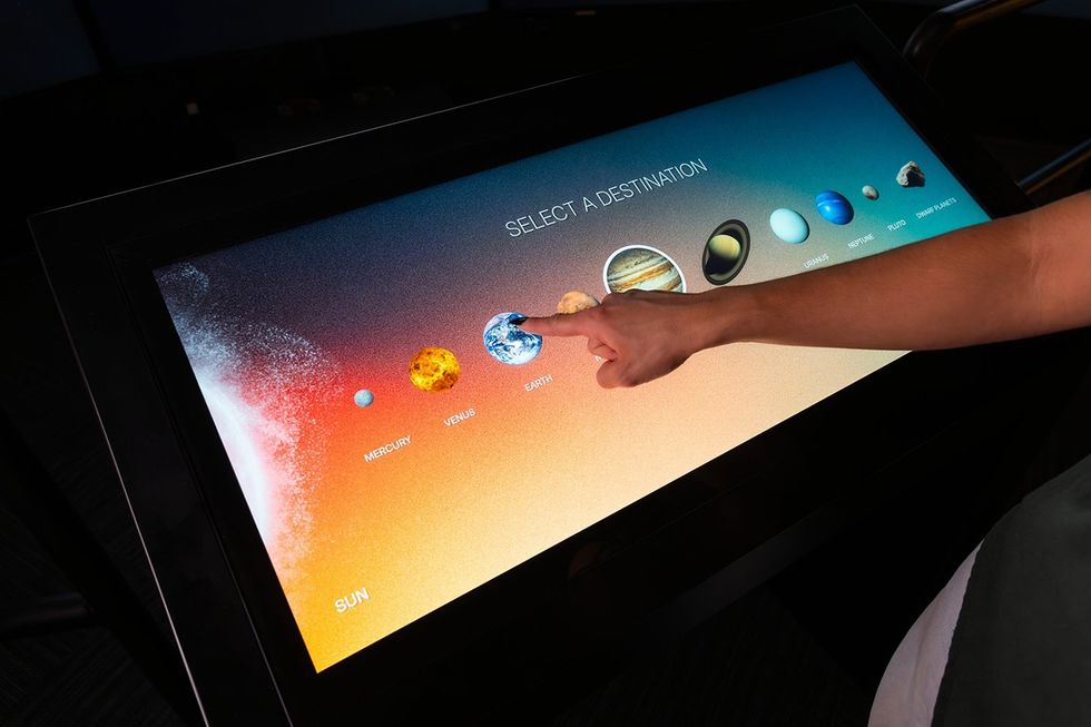 Touchscreen displaying planets; a hand points to Earth, labeled "Select a Destination."