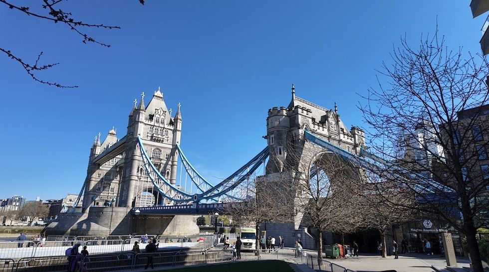 Tower Bridge in London under a clear blue sky, surrounded by trees and people.