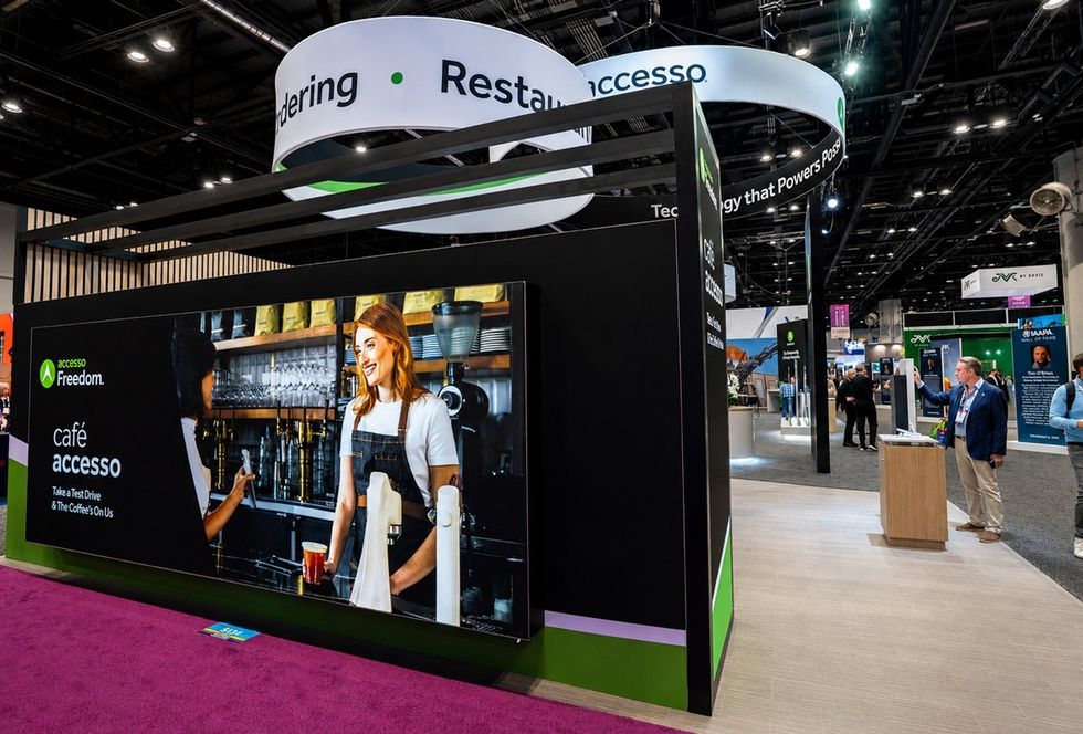 Trade show booth with a large caf\u00e9-themed display and interactive technology exhibits.