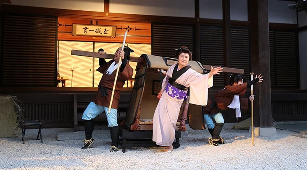 Traditional Japanese sedan chair with a person and two carriers in historical attire.
