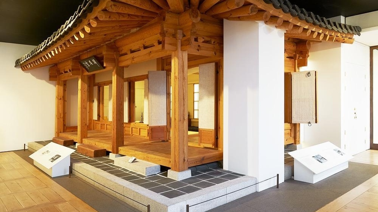 Traditional wooden Korean structure exhibit with tiled roof in a museum setting