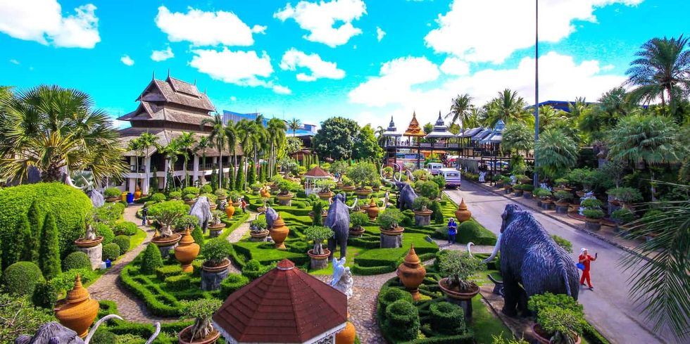 Tropical garden with statues, lush greenery, and traditional Thai architecture under a blue sky - Nong Nooch Tropical Botanical Garden