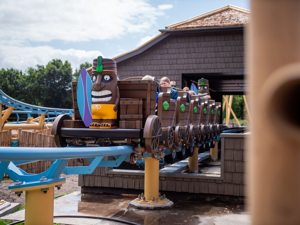 Tropical-themed roller coaster with tiki head cars on blue tracks.
