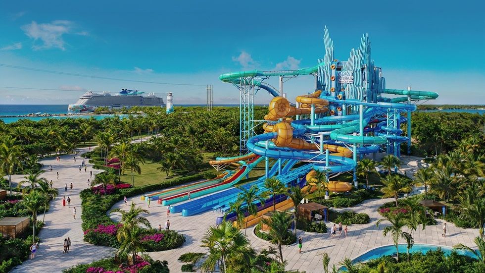 Tropical water park with slides, cruise ship in the background, palm trees, and clear skies.