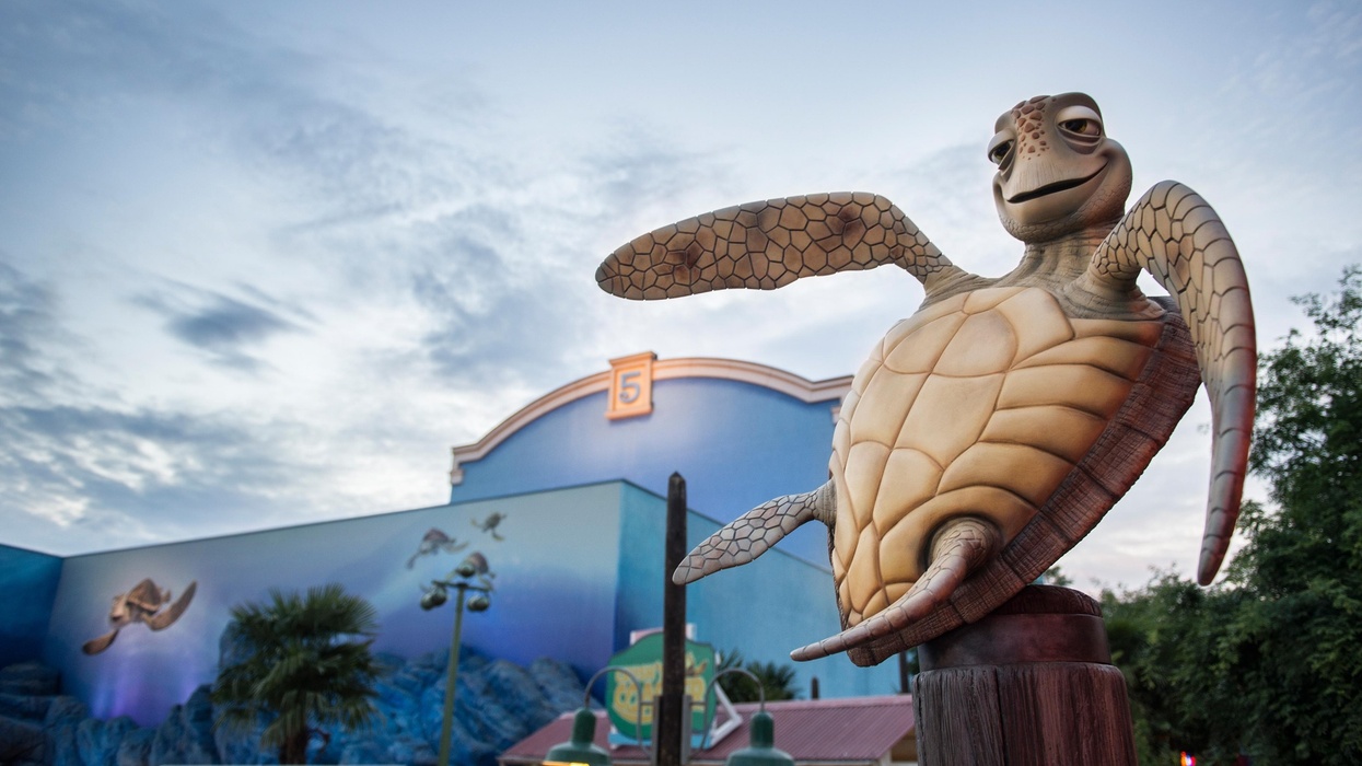 Turtle statue in Disneyland Paris, blue building with murals in the background under cloudy sky.