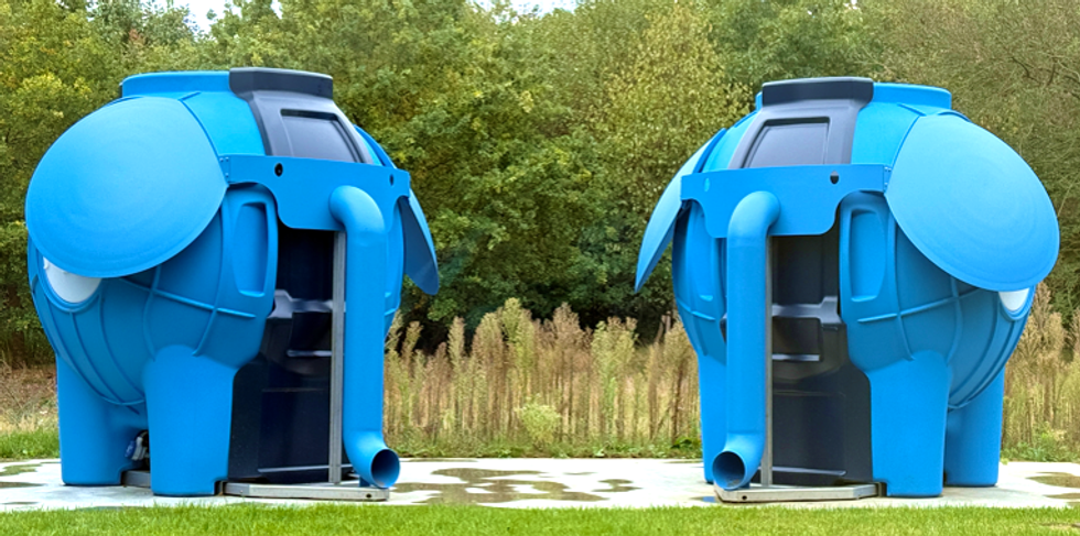 Two blue elephant-shaped structures in a grassy area with trees in the background.