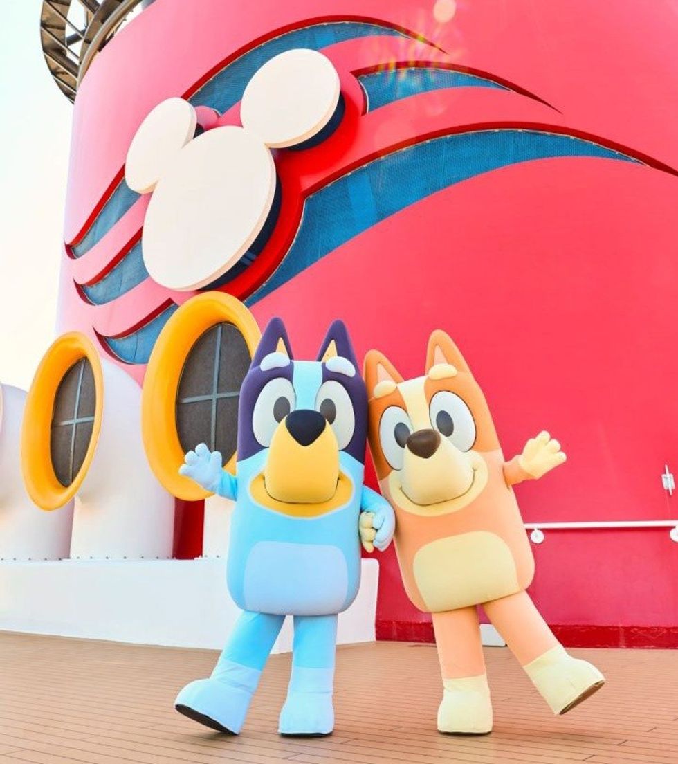 Two Bluey mascots posing on a cruise ship with a Mickey Mouse logo.