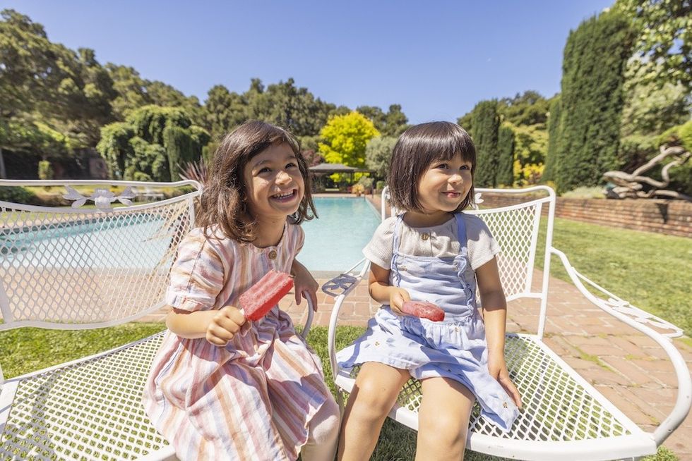 Two children eating popsicles on a sunny day by the pool.