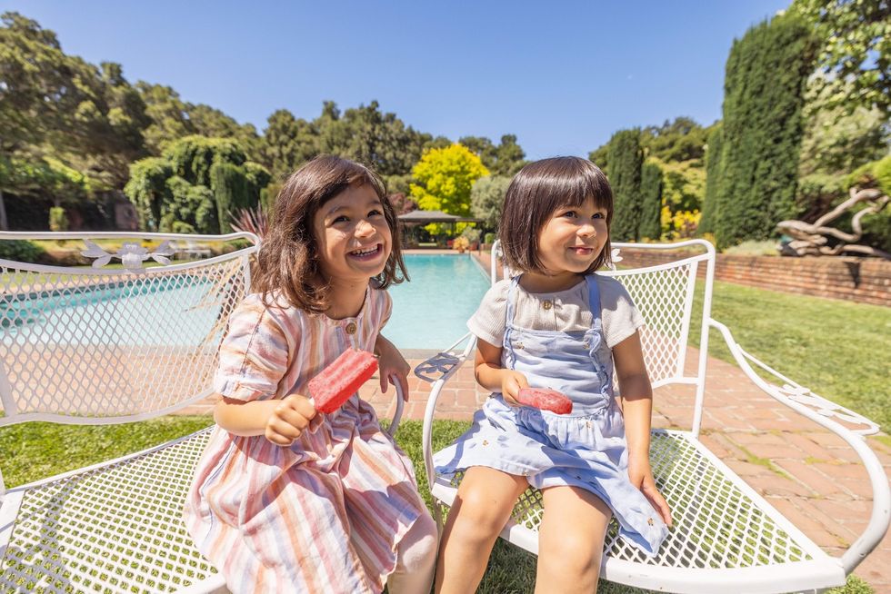 Two children enjoying popsicles by a pool on a sunny day.