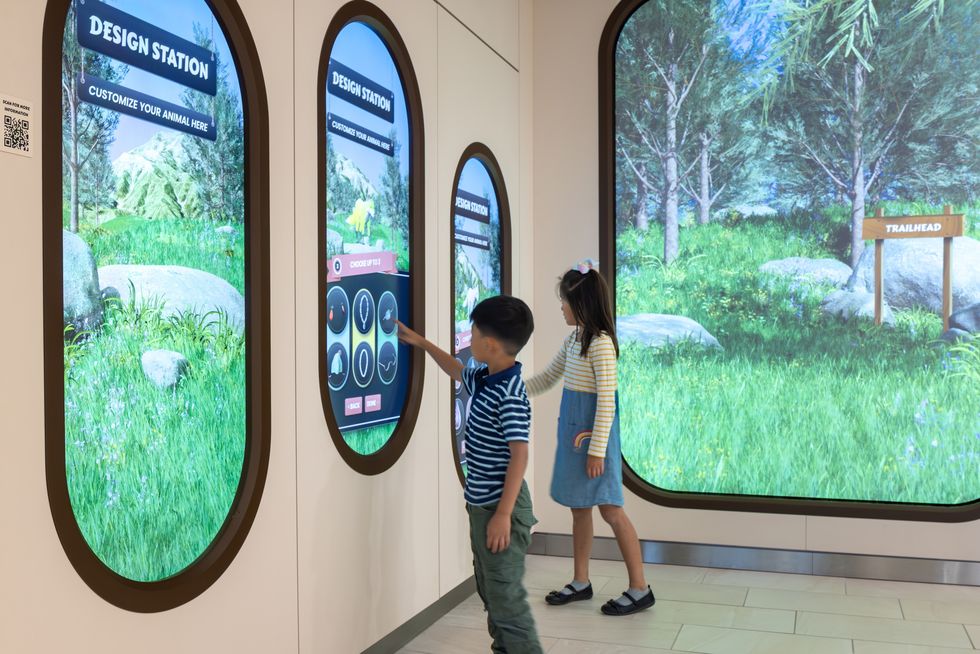 Two children use interactive animal-design screens in a nature-themed exhibit.