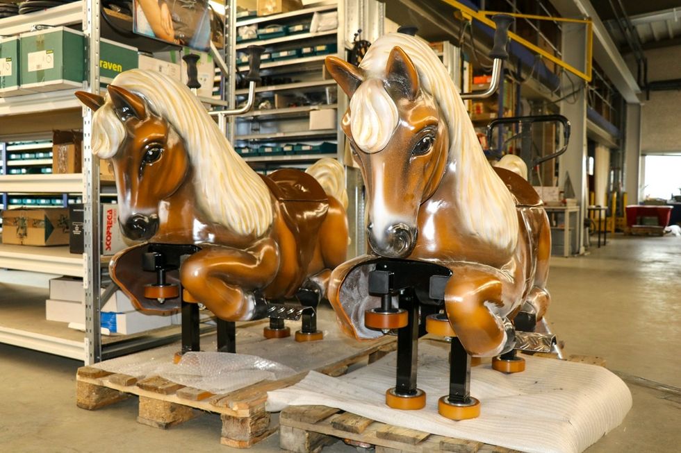 Two coin-operated horse rides on wooden pallets in a warehouse.