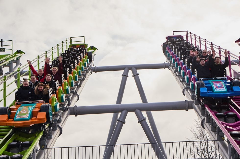 Two colorful roller coasters ascending, riders excitedly raise their hands.