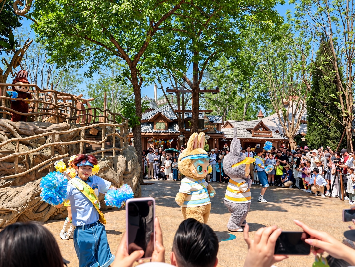 Two costumed rabbit characters and a cheerleader perform for a crowd at a sunny theme park.