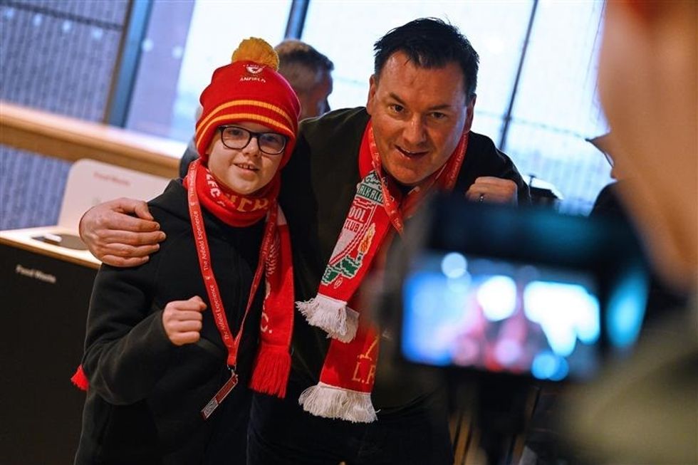 Two fans wearing Liverpool scarves and hats, posing for a photo indoors.