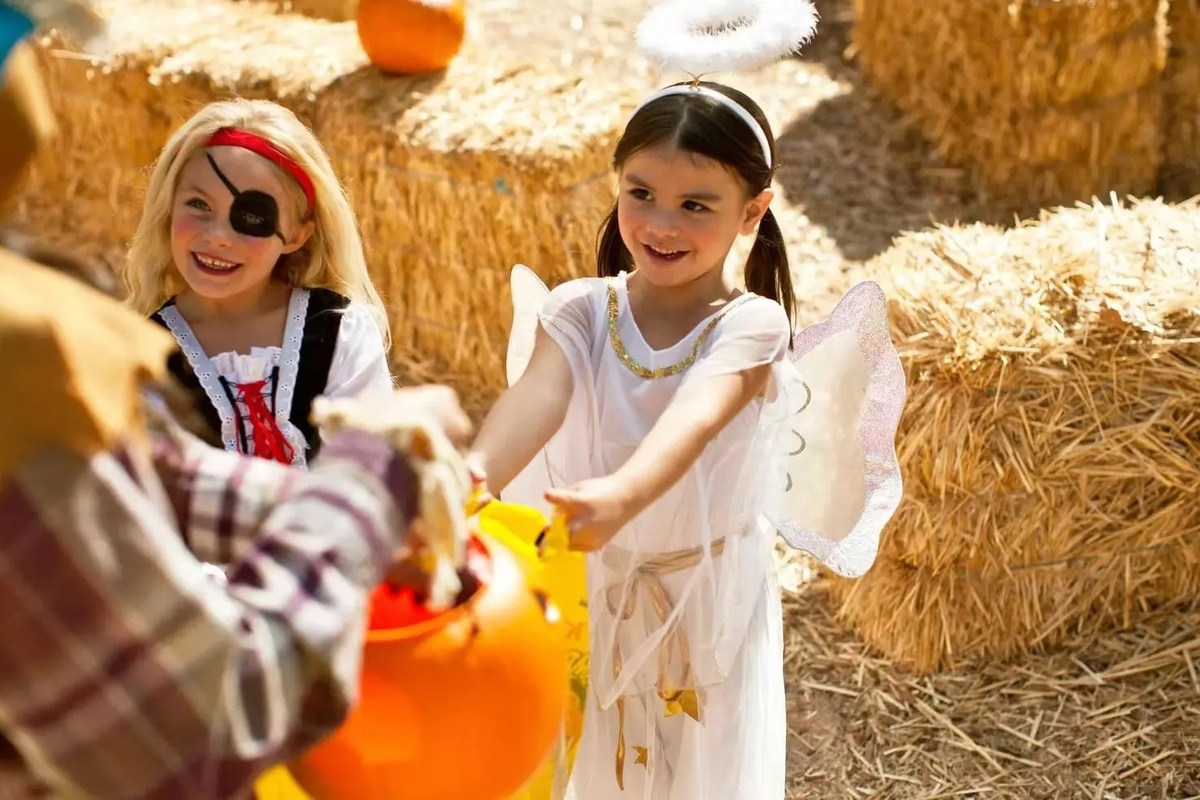 Two girls, dressed as an angel and pirate, trick-or-treat near hay bales at Six Flags Darien Lake