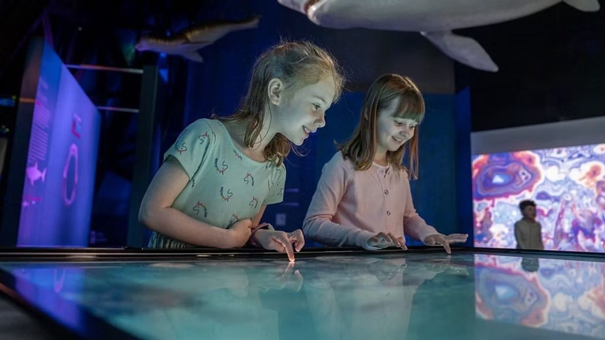 Two girls interact with a Breeze Creative touchscreen display in a colorful, museum exhibit.