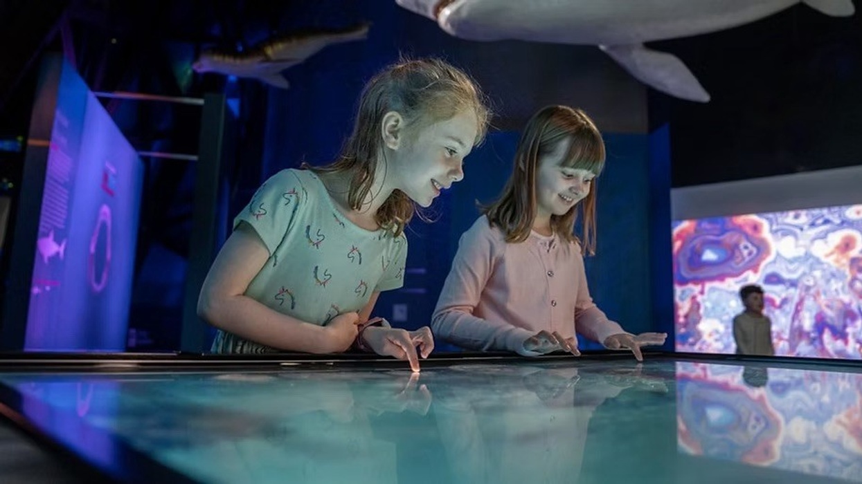 Two girls interact with a Breeze Creative touchscreen display in a colorful, museum exhibit.