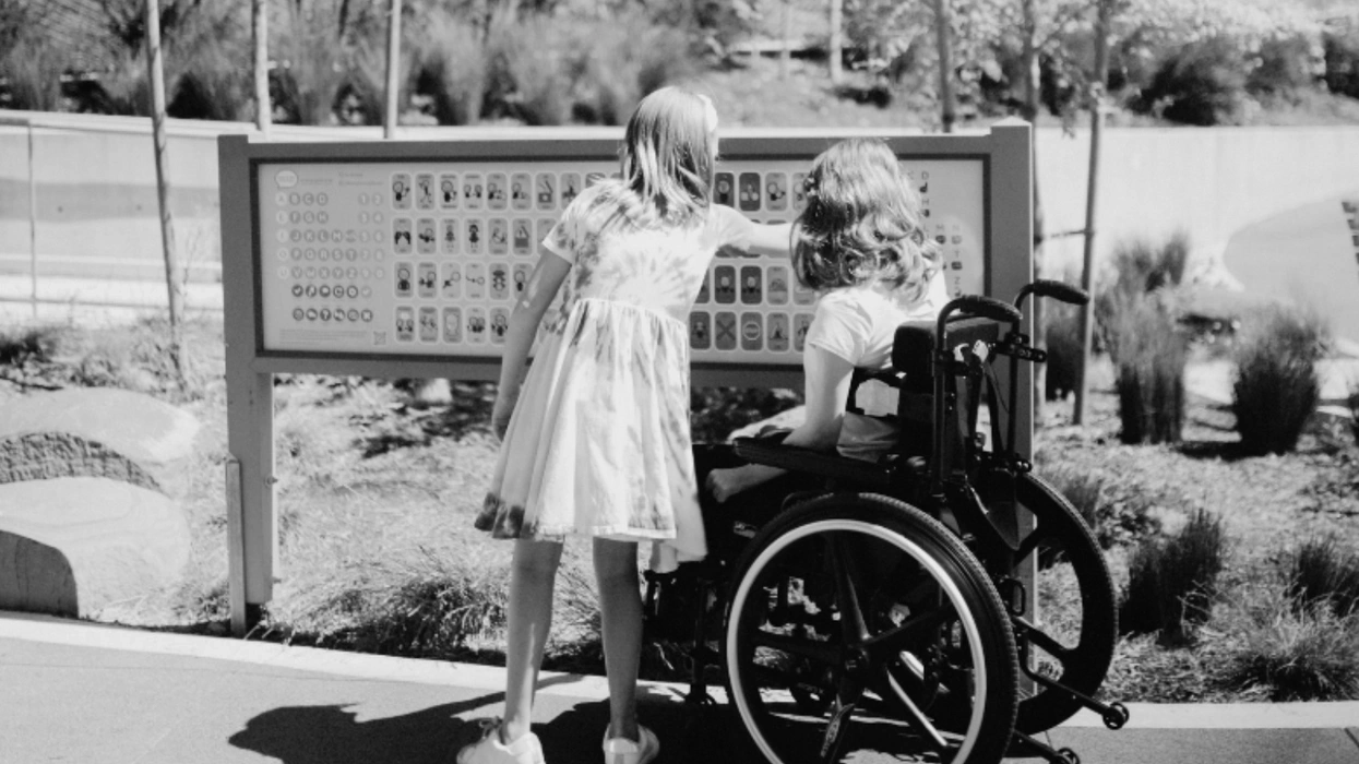 Two girls, one in a wheelchair, explore a tactile sign in a park.