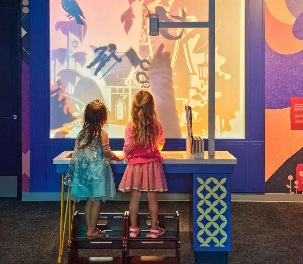 Two girls play with shadow figures on a colorful interactive wall display at Kaleideum