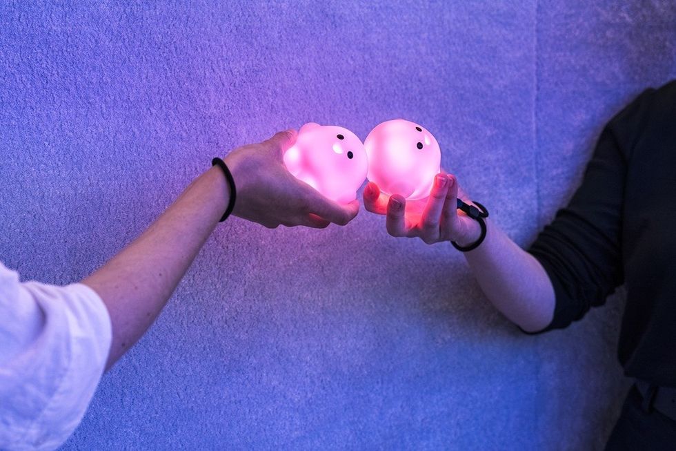 Two hands holding glowing pink blobs against a blue wall.